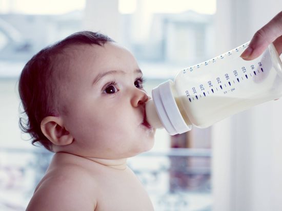 Ein sitzendes Kleinkind trinkt Milch aus einem Fläschchen.