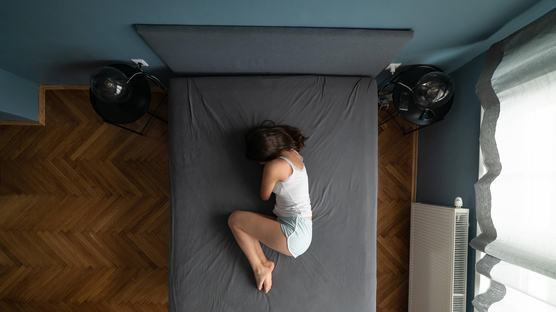 Eine Frau liegt mit angewinkelten Beinen seitlich auf einem Bett. 