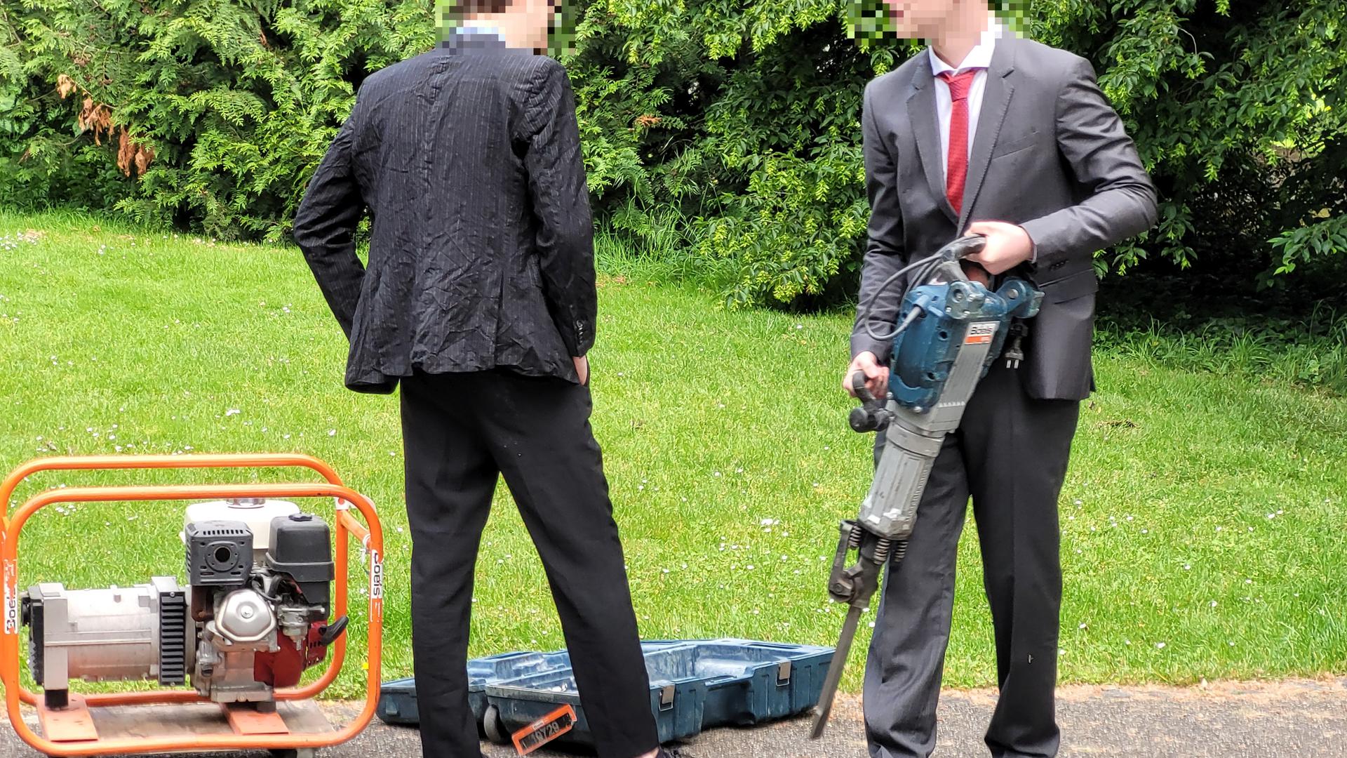 Zwei junge Männer im Anzug und mit Bohrhammer.