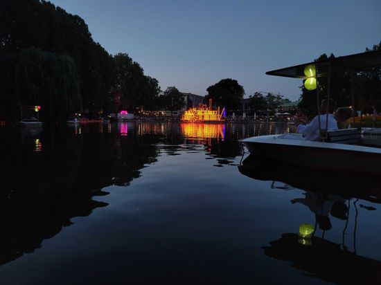 Blick auf den See im Karlsruher Zoo. Im Hintergrund ein leuchtender Mississippi-Dampfer.
