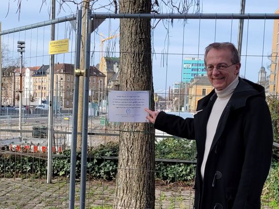Pfarrer Rainer Auer am Durlacher Tor, zeigt auf ein Schild, das vor der Fällung eines Baumes warnt.