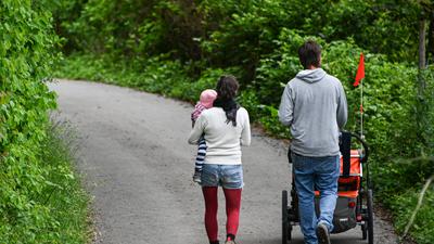 Ein Paar mit Kind läuft eine schmale Straße entlang, die auf beiden Seiten bewachsen ist.