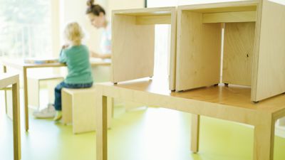 Eine Erzieherin und ein Kind spielen in einem städtischen Kindergarten hinter auf den Tisch gestellten Stühlen. (zu dpa: «Immer mehr unter Dreijährige in Kita oder von Tageseltern betreut») +++ dpa-Bildfunk +++