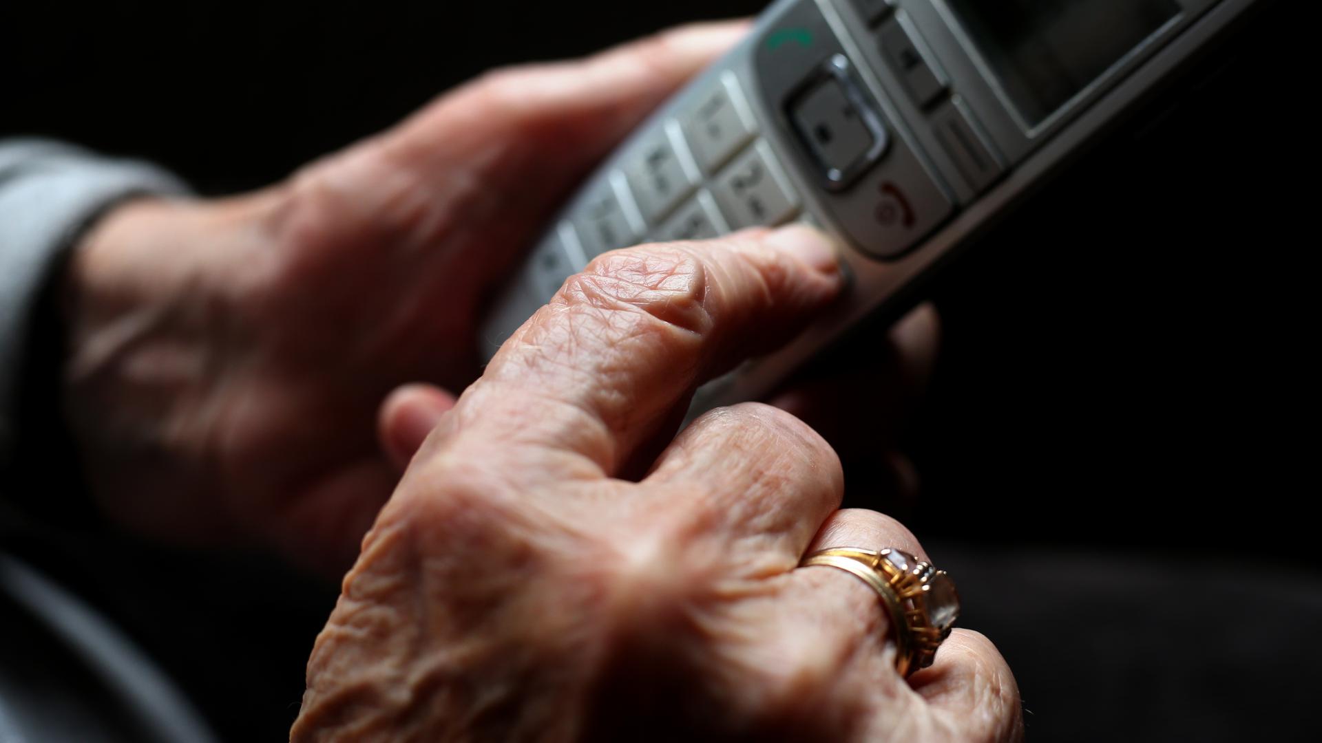 Eine ältere Frau tippt auf einem schnurlosen Festnetztelefon. 