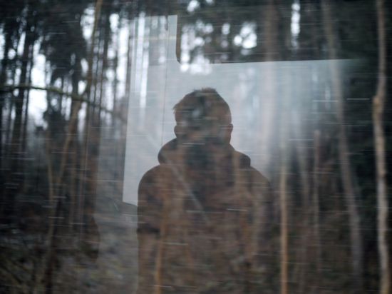 Ein Spiegelbild eines Menschen, der aus einem Fenster in Richtung Wald blickt.