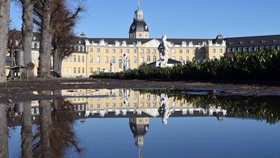 Außenaufnahme des Karlsruher Schlosses, das sich in einer Pfütze spiegelt.