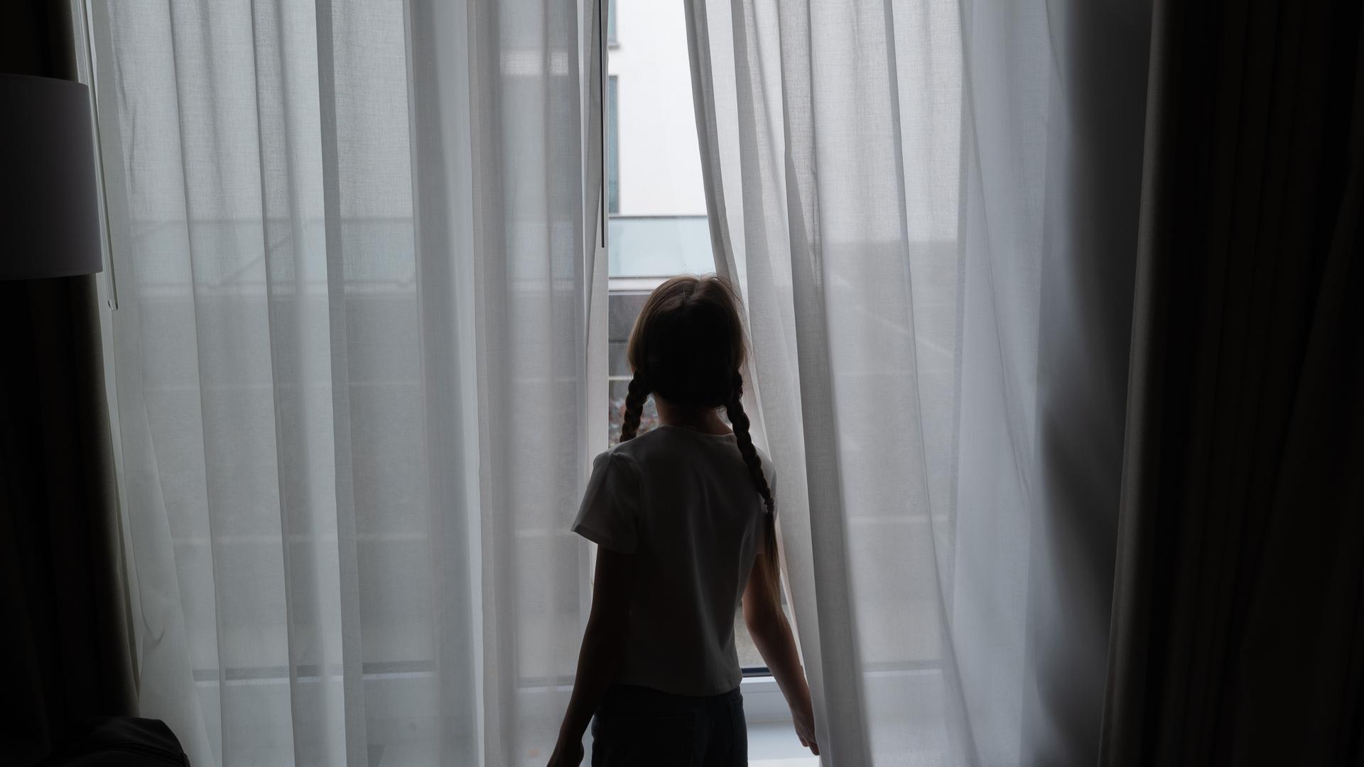 Ein Kind steht in einem Hotel an einem Fenster. 