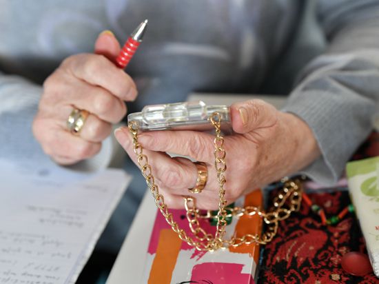 Eine Seniorin hält ihr mit einer goldenen Kette versehenes Smartphone in den Händen. (zu dpa "Enkeltrick» per Handynachricht - Wie man sich vor Betrügern schützt") +++ dpa-Bildfunk +++