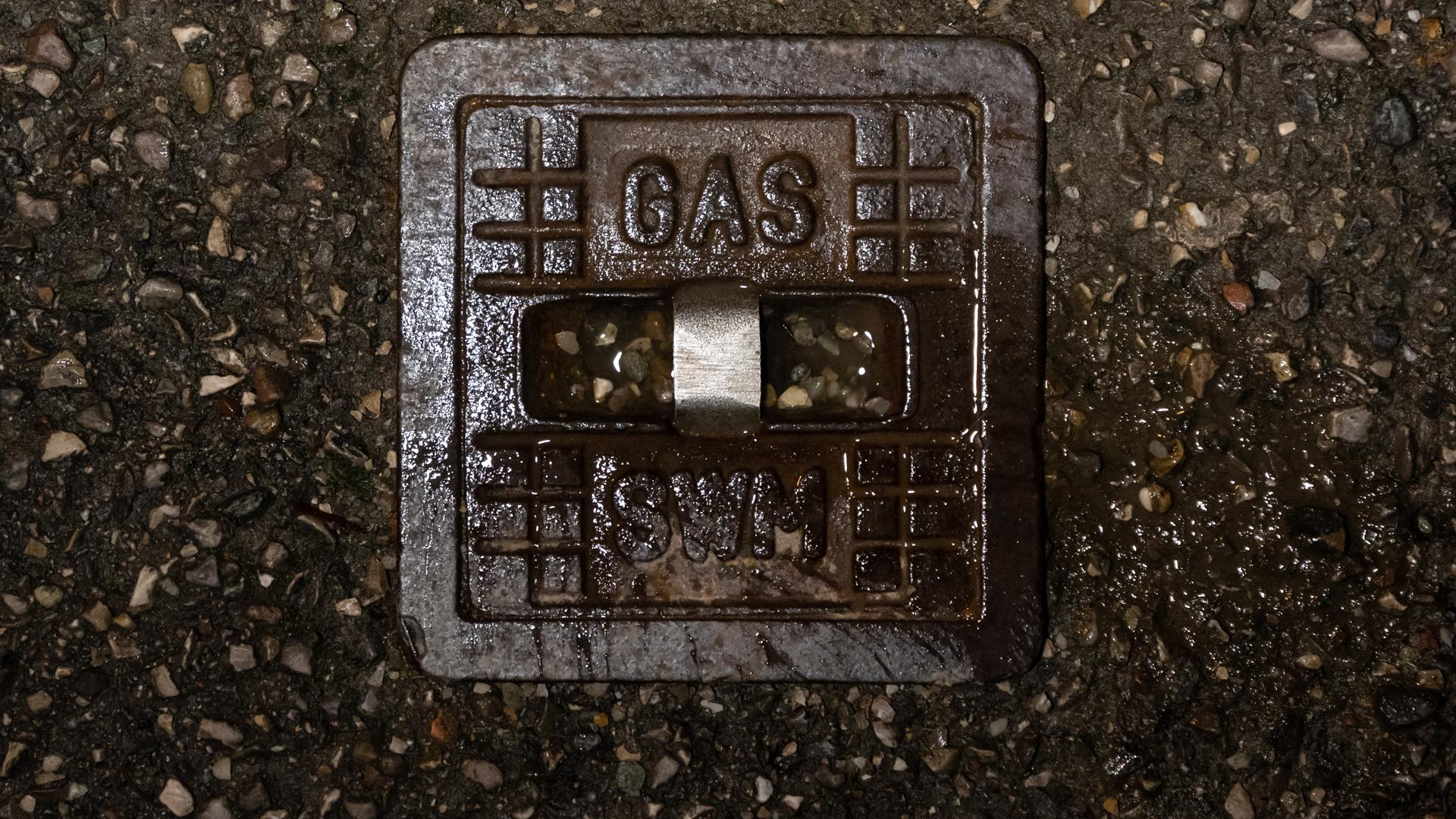Der Schriftzug „Gas“ steht in einem Wohngebiet auf einer gusseisernen Straßenkappe einer Gasleitung. +++ dpa-Bildfunk +++