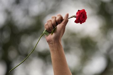 Eine Frau hebt während einer Demonstration anlässlich des Internationalen Frauentags ihre geballte Faust und hält eine rote Rose. 