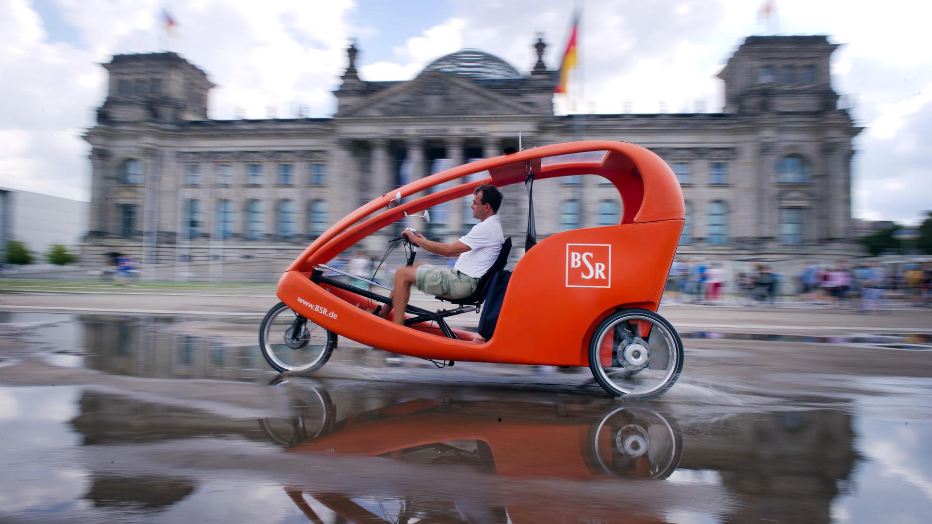Der Fahrradtaxi-Fahrer Golo Kohl fährt am 14.08.2014 in Berlin durch eine Pfütze vor dem Reichstag. Foto: Daniel Naupold/dpa ++ +++ dpa-Bildfunk +++