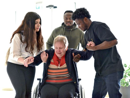Drei junge Leute helfen einer älteren Frau aus dem Rollstuhl