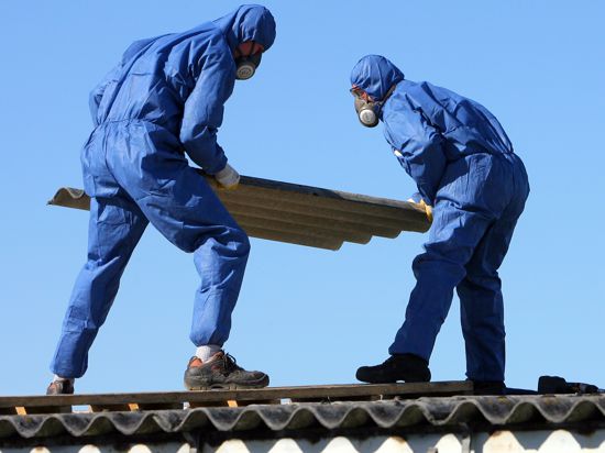 Arbeiter mit Schutzanzügen tragen eine Asbestplatte