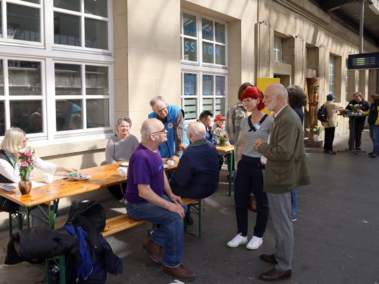 Blick auf die Bahnhofsmission in Karlsruhe, Menschen sitzen auf Bierbänken und reden