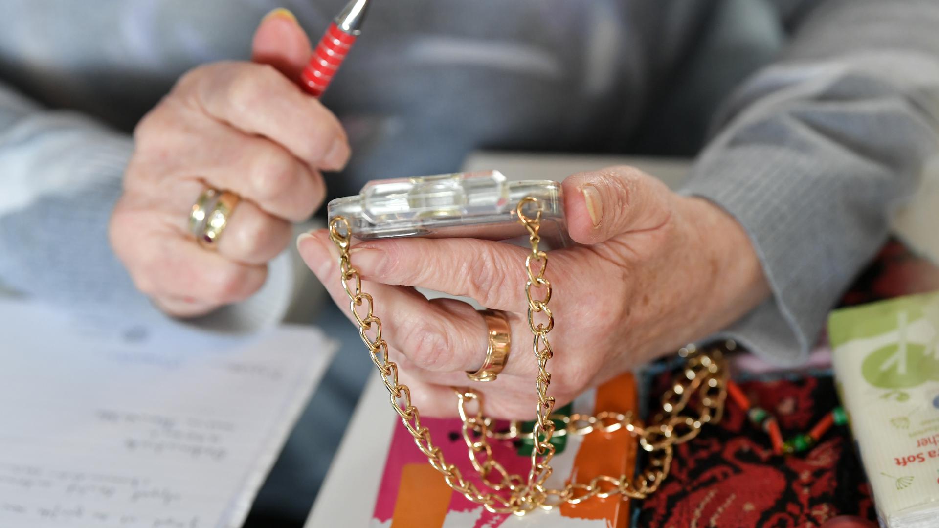 Eine Seniorin hält ihr mit einer goldenen Kette versehenes Smartphone in den Händen.
