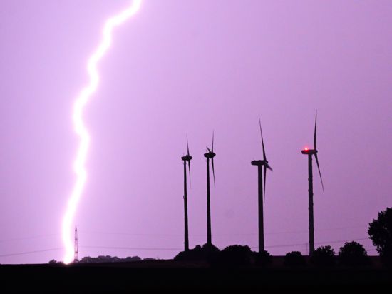 Ein Blitz entlädt sich während eines Gewitters hinter Windrädern.