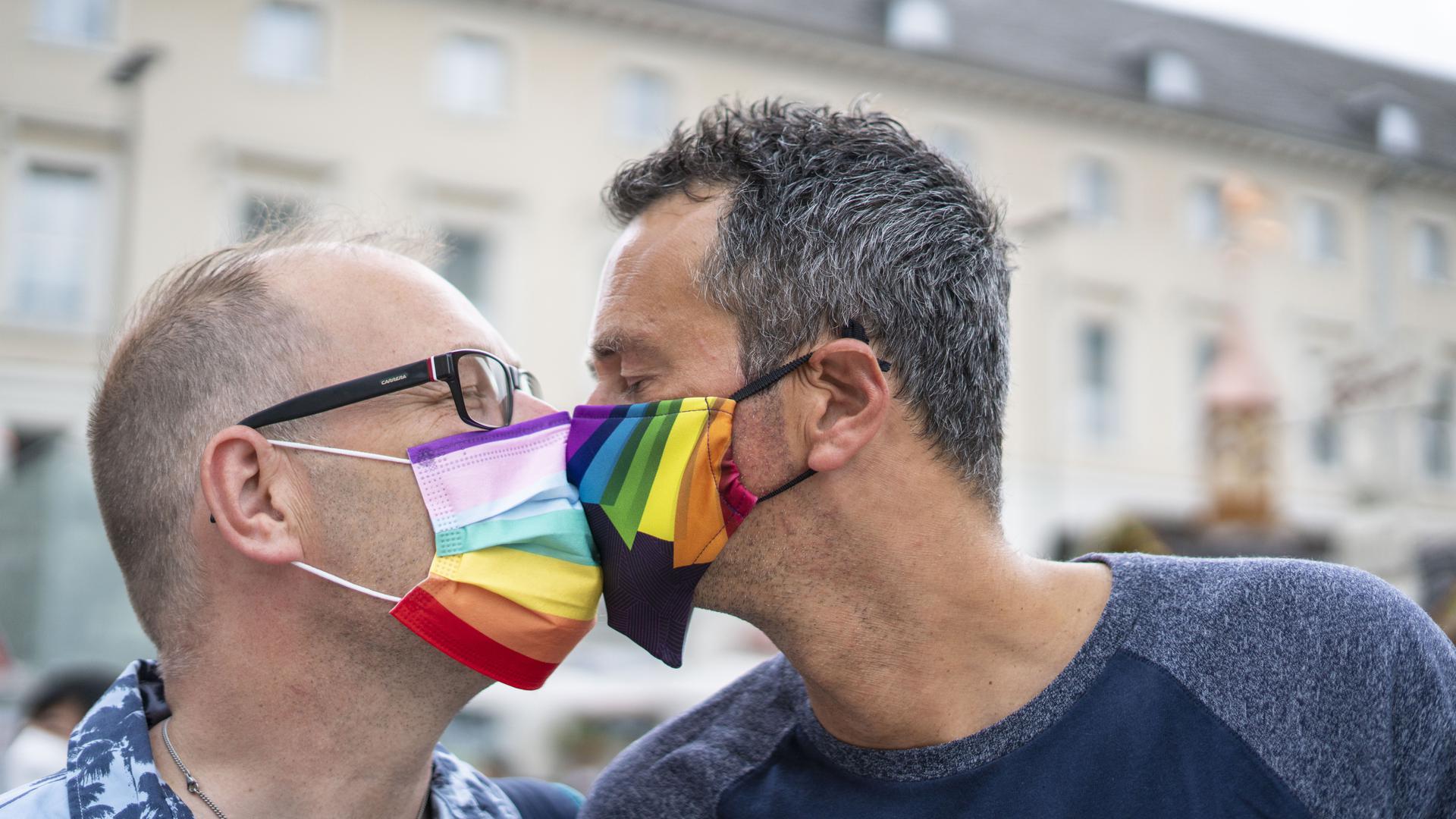 Zwei Männer mit Regenbogenmaske küssen sich.