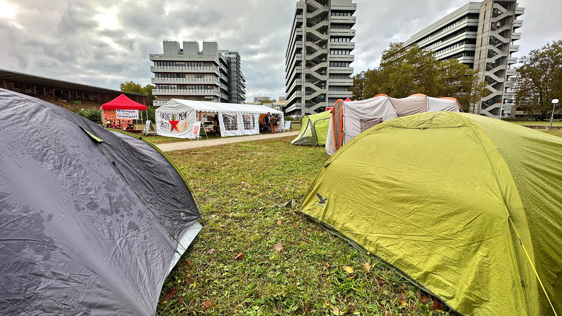 Das Protestcamp befindet sich auf einer Wiese auf dem Campus Süd des Karlsruher Instituts für Technologie (KIT), im Hintergrund sind Universitätsgebäude zu erkennen.