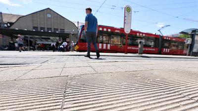 Am 28.06.2022 überquert ein Mensch den Platz vor dem Haupteingang des Hauptbahnhofs Karlsruhe und die geriffelten Bodenelemente des Blindenleitsystems.