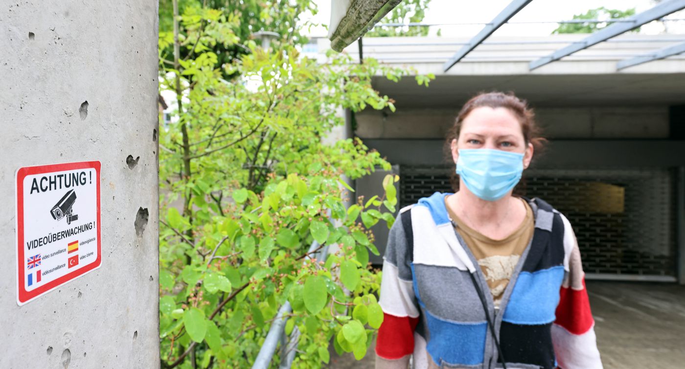 Eine Frau mit Mundschutzmaske steht vor der Einfahrt einer Tiefgarage.