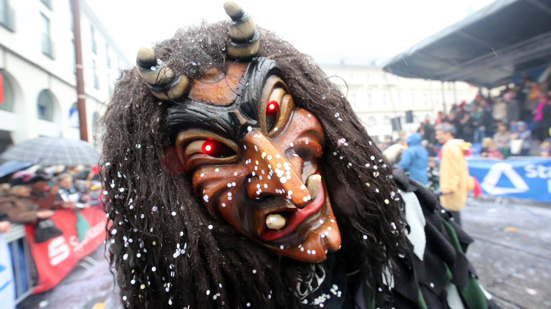 Im Konfettiregen zieht ein Fastnachter mit alemannisch inspirierter Maske im Februar 2020 beim traditionellen Umzug durch die Karlsruher City an der Zuschauertribüne vorbei.