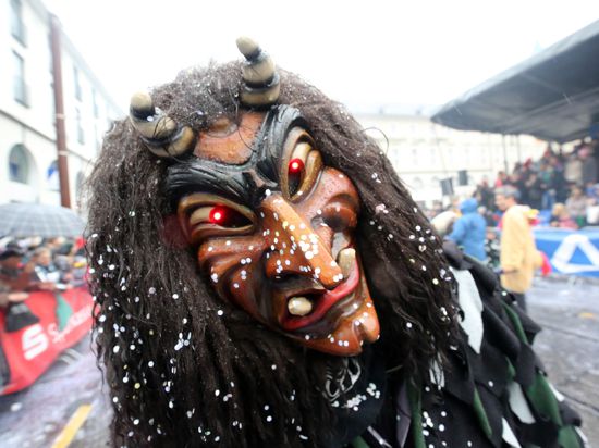 Im Konfettiregen zieht ein Fastnachter mit alemannisch inspirierter Maske im Februar 2020 beim traditionellen Umzug durch die Karlsruher City an der Zuschauertribüne vorbei.