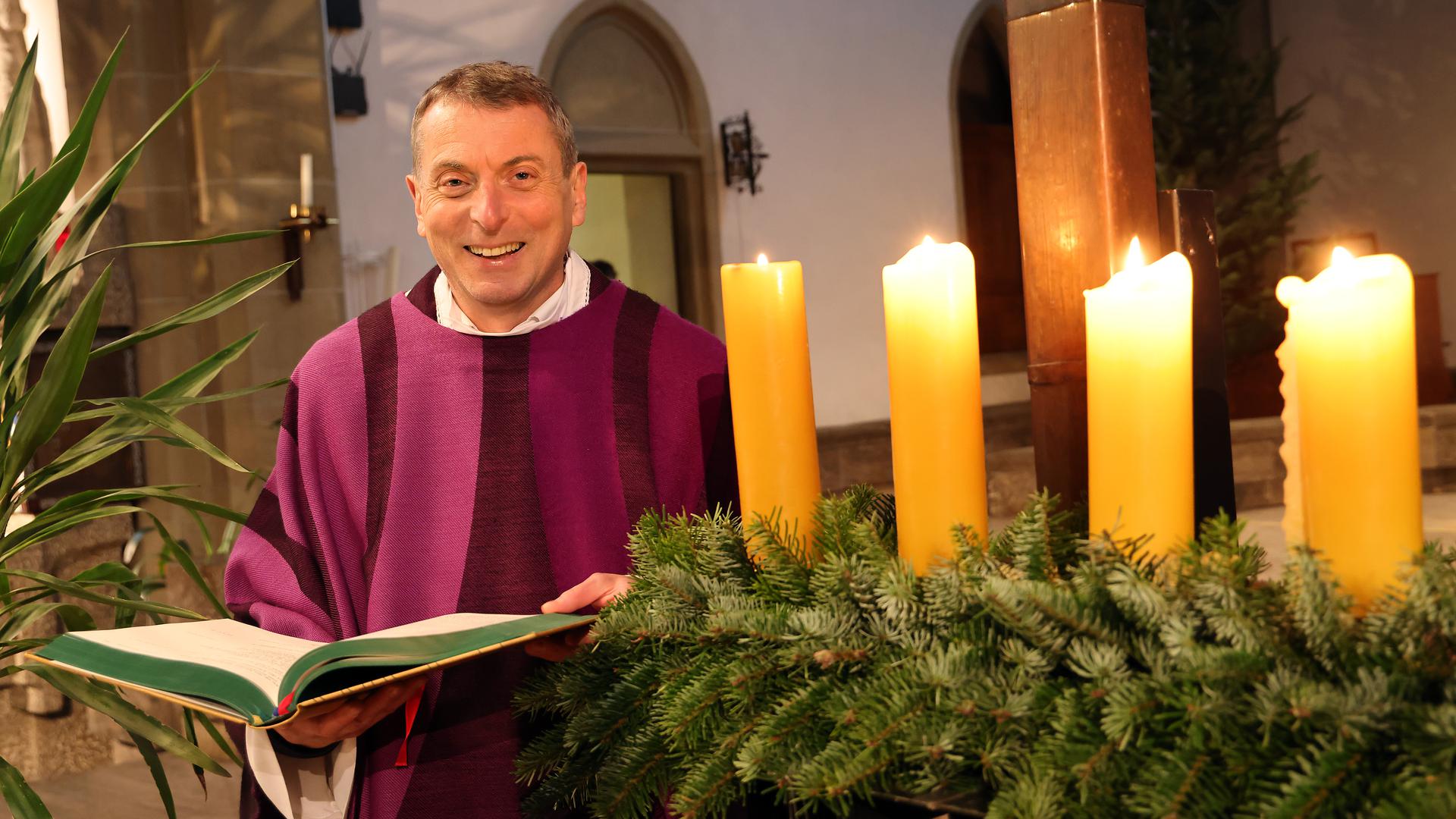 Priester Alexander Hafner von der Karlsruher Seelsorgeeinheit Allerheiligen steht kurz vor Weihnachten neben einem Adventskranz.