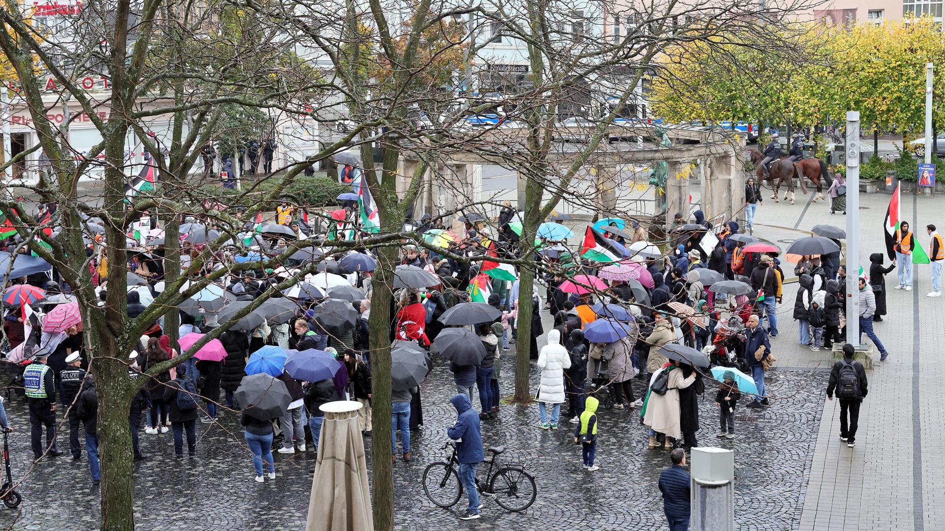 Blick auf rund 280 Teilnehmer einer Kundgebung auf dem Stephanplatz mit Regenschirmen und Palästina-Flaggen.