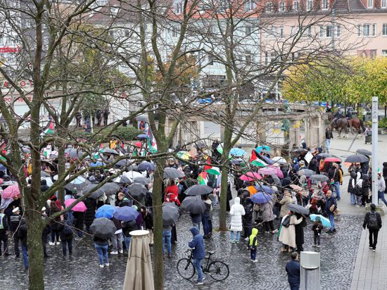 Blick auf rund 280 Teilnehmer einer Kundgebung auf dem Stephanplatz mit Regenschirmen und Palästina-Flaggen.