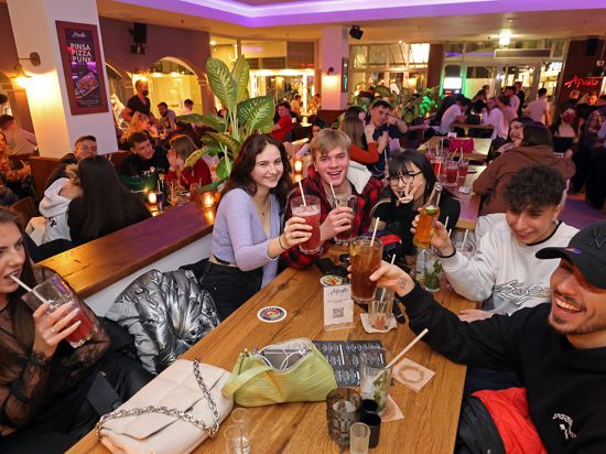 Eine Gruppe lachender junger Leute sitzt an einem Tisch im „Aposto“ in Karlsruhe und stößt mit Cocktails an.