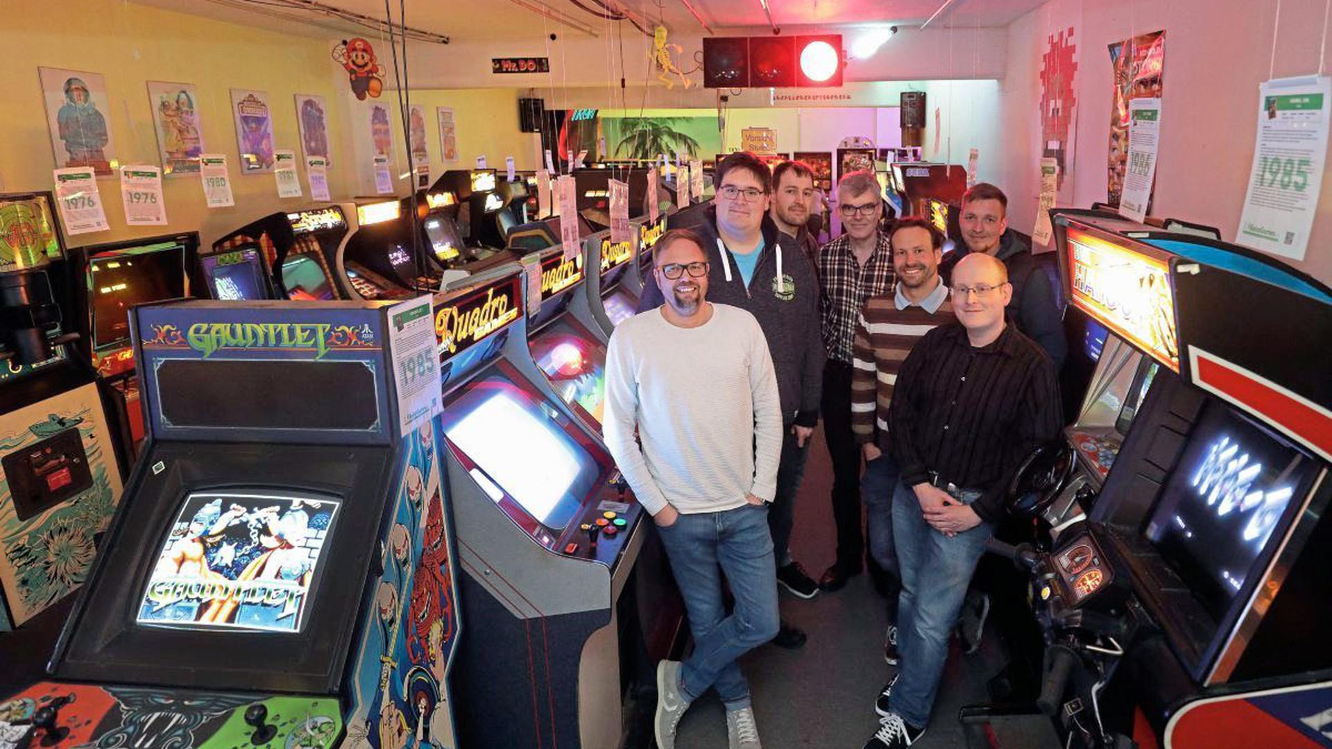 Sieben Männer in einem Raum voller Arcade-Automaten