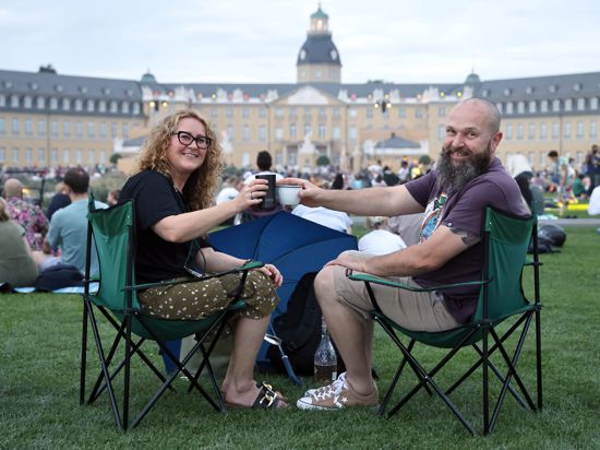 Zwei Menschen sitzen in Campingstühlen auf der Wiese vor dem Karlsruher Schloss.