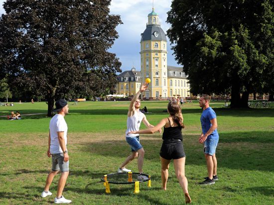 Vier junge Leute spielen vor dem Karlsruher Schloss Spikeball. 