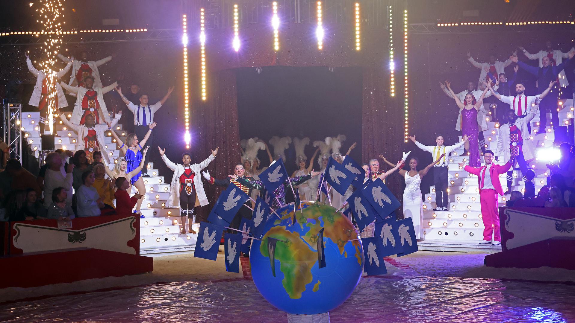 Ein großer Globus mit vielen Fahnen mit Friedenstauben und im Hintergrund den Artisten