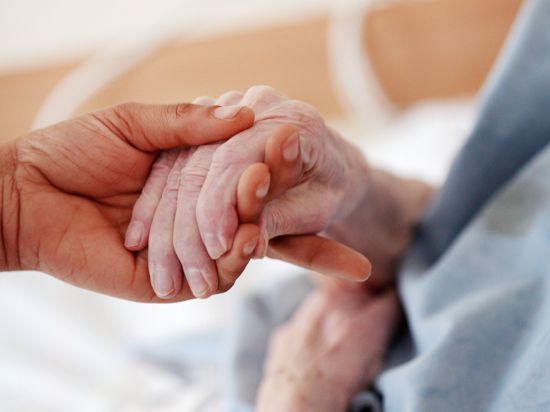 Eine Pflegerin hält in einem Altenheim die Hand einer Bewohnerin. 