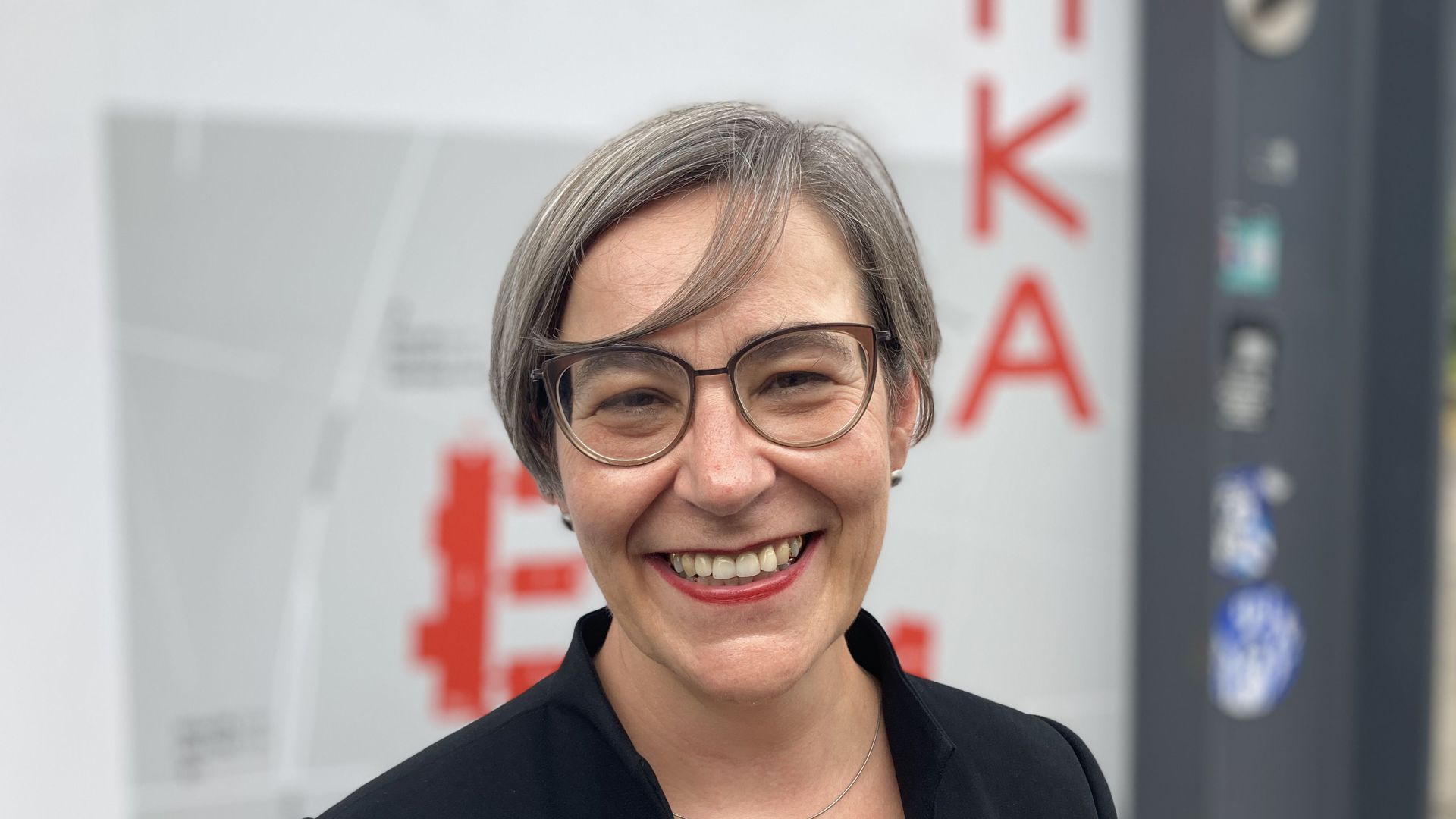 Rose Marie Beck, die neue Rektorin der Hochschule Karlsruhe, steht lachend vor dem Lageplan des Campus.