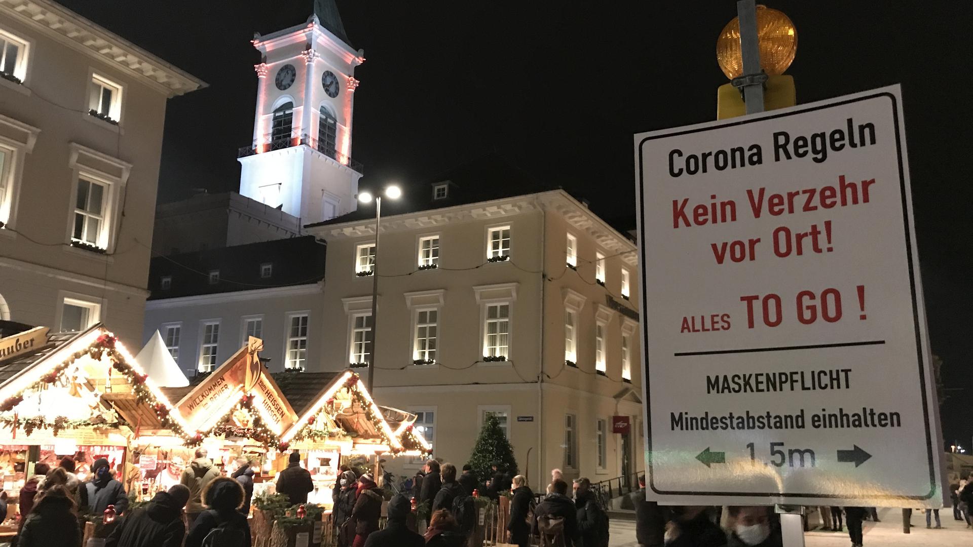 Ein Schild weist auf dem Karlsruher Mini-Weihnachtsmarkt auf die Maskenpflicht und das Verzehrsverbot auf dem Marktplatz hin. Mit Lautsprecherdurchsagen und persönlichen Ansprachen haben Polizei und Ordnungskräfte Menschenansammlungen und kleinere Gruppen zum Gehen aufgefordert.