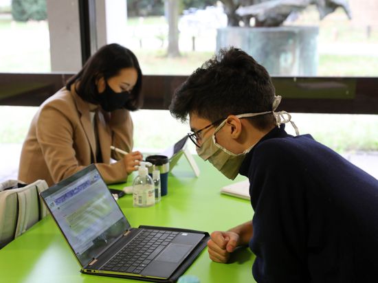 Zwei Studierende sitzen sich mit Masken am Laptop gegenüber.