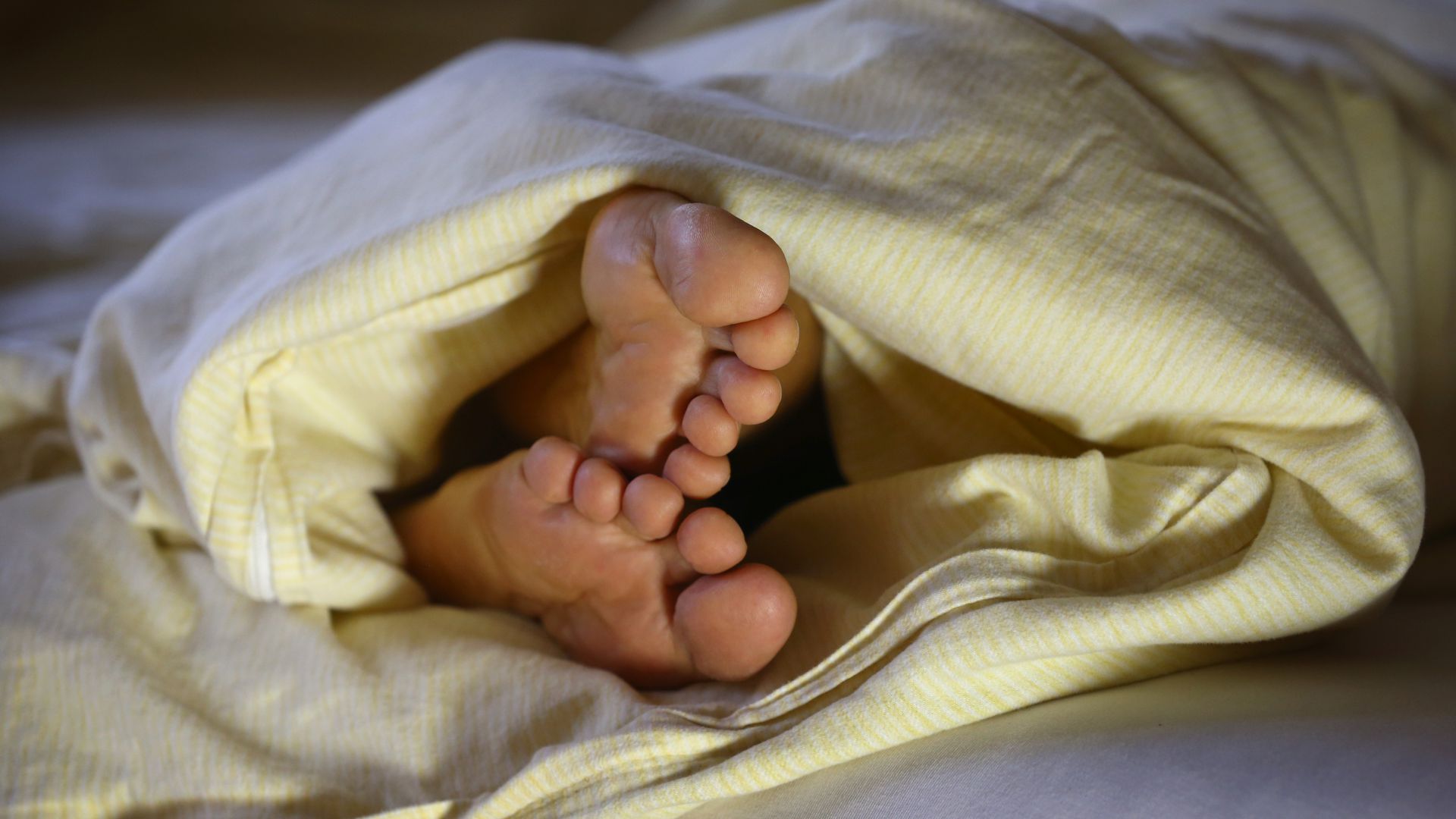 Die Füße einer schlafenden Frau ragen unter einer Bettdecke hervor. 