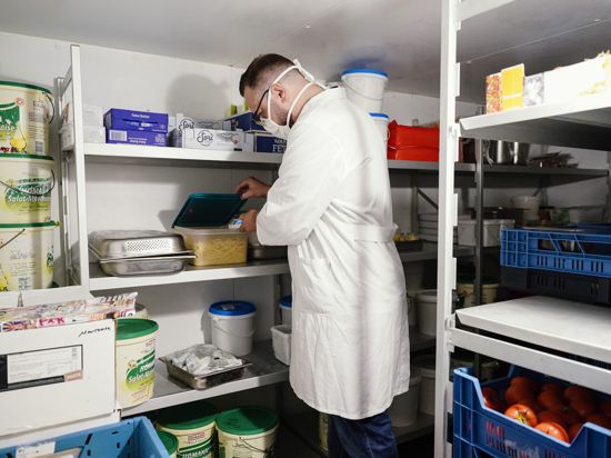 Lebensmittelkontrolleur kontrolliert mit einem Thermometer eine Box mit Nudeln im Kühlhaus eines Restaurants. 