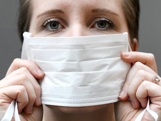 Eine Frau hält einen Mundschutz vor ihrem Gesicht. 