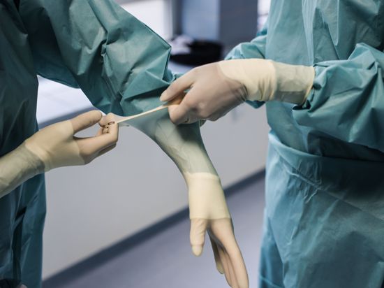 Eine Ärztin zieht sich im Operationssaal Handschuhe an. 