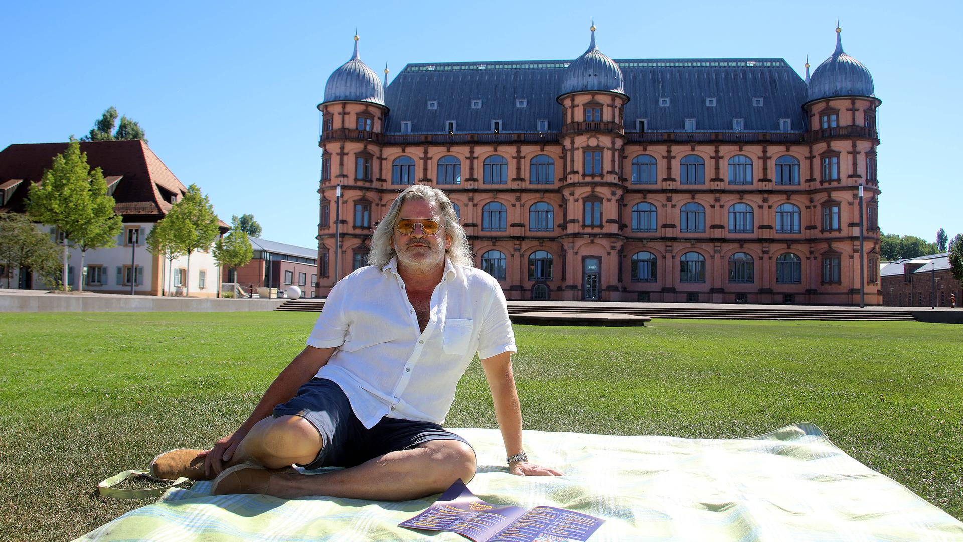 Schauburg-Chef Herbert Born sitzt vom dem Schloss Gottesaue auf einer Picknick-Decke.