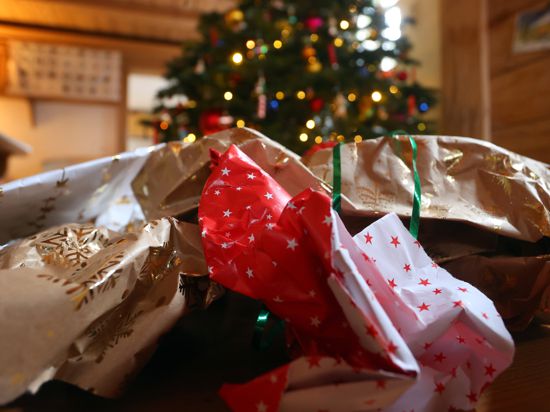 Geschenkpapier von ausgepackten Weihnachtsgeschenken liegt auf dem Boden eines Zimmers vor einem geschmücktem Weihnachtsbaum.
