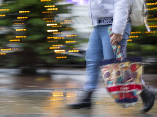 Eine Frau mit einer Einkaufstasche geht über eine Einkaufsstraße.