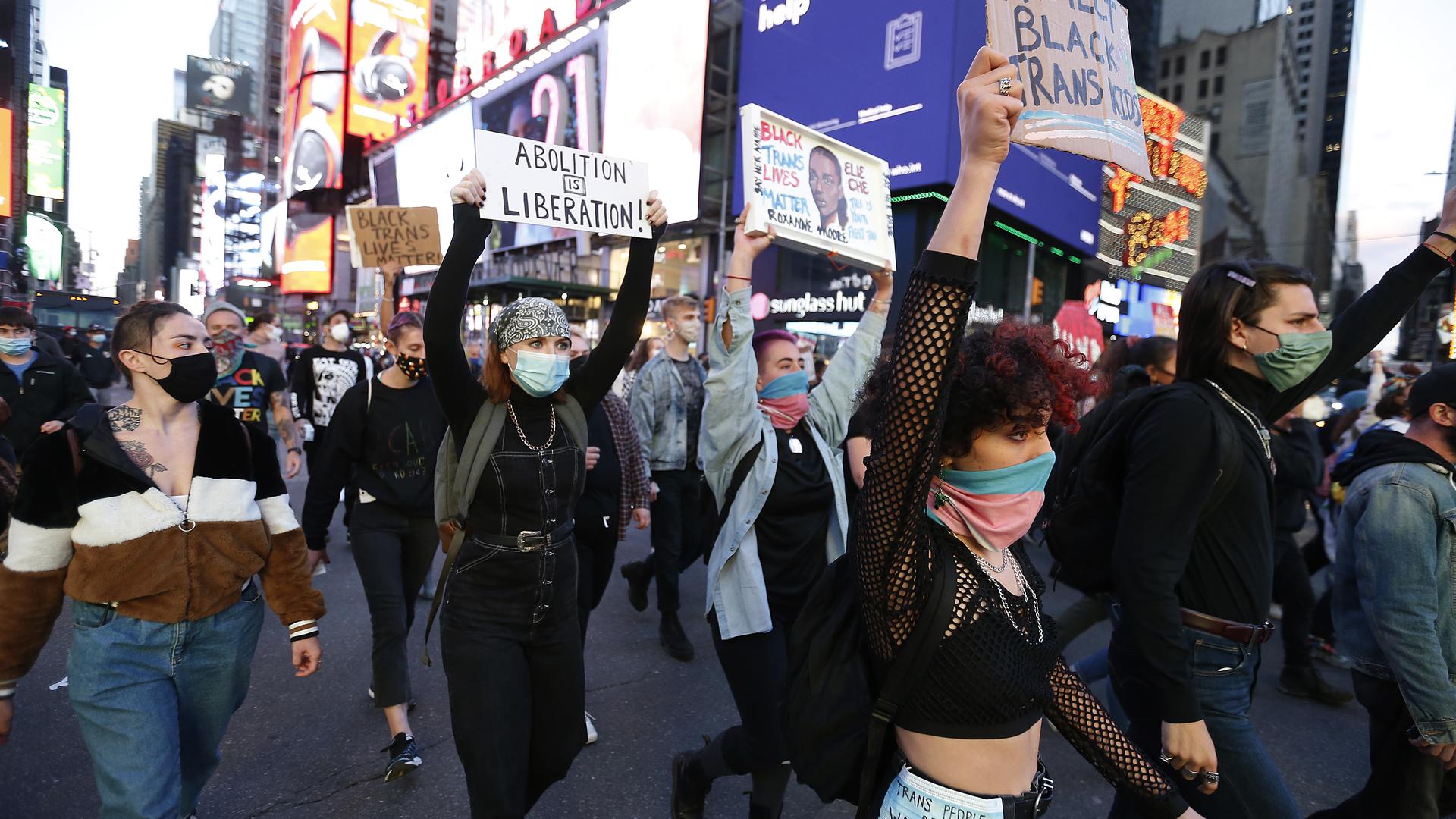 Demonstranten tragen während einer Protestaktion Mund-Nasen-Schutz und heben Plakate in die Luft. 
