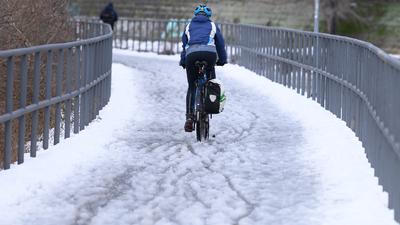 Eine Radfahrerin fährt auf einem verschneiten Radweg entlang. +++ dpa-Bildfunk +++