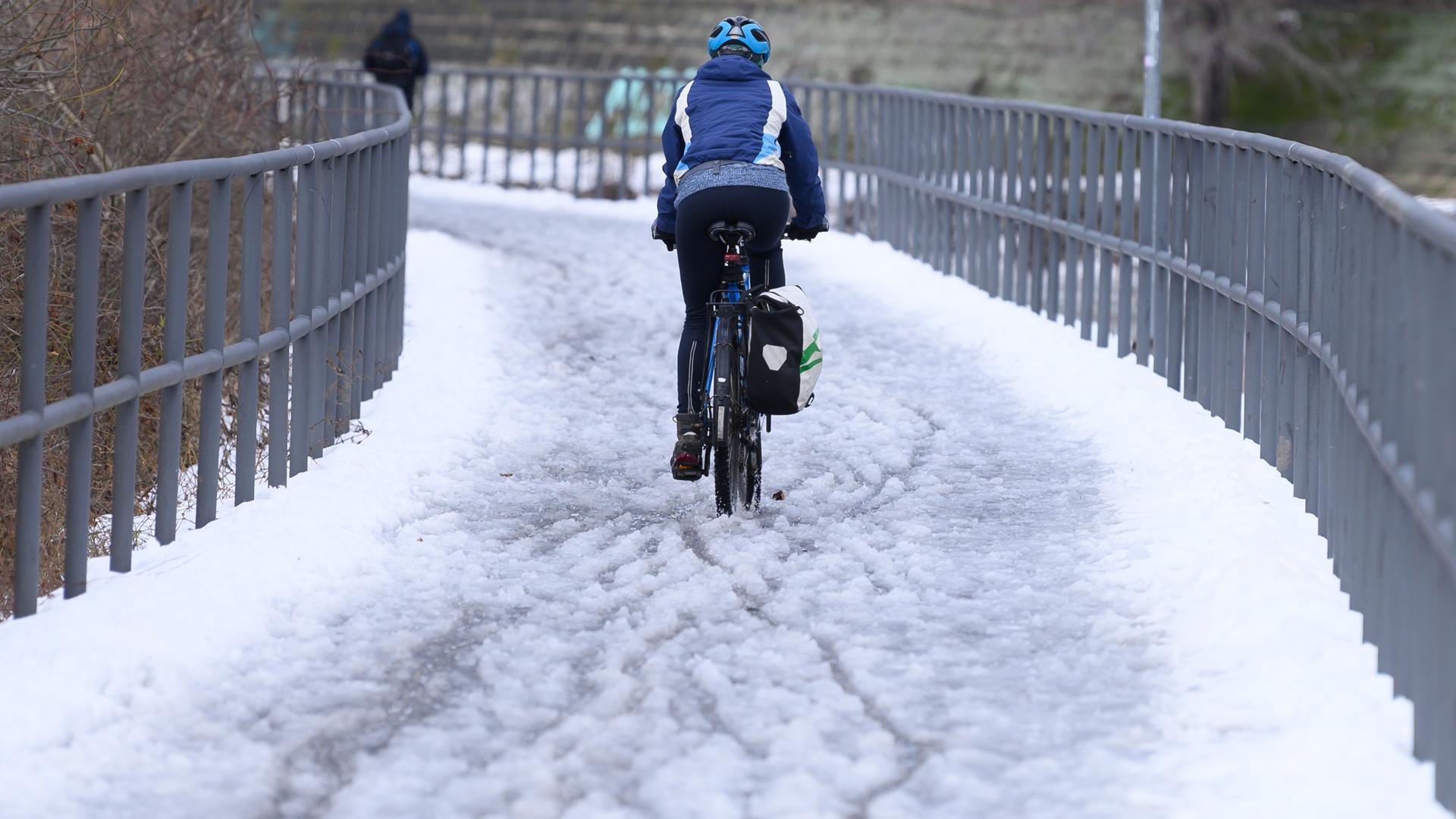 Eine Radfahrerin fährt auf einem verschneiten Radweg entlang. 