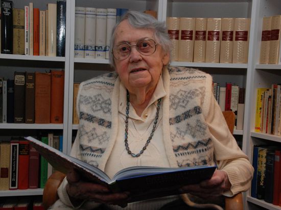 Eine ältere Frau mit Brille hält ein Buch.