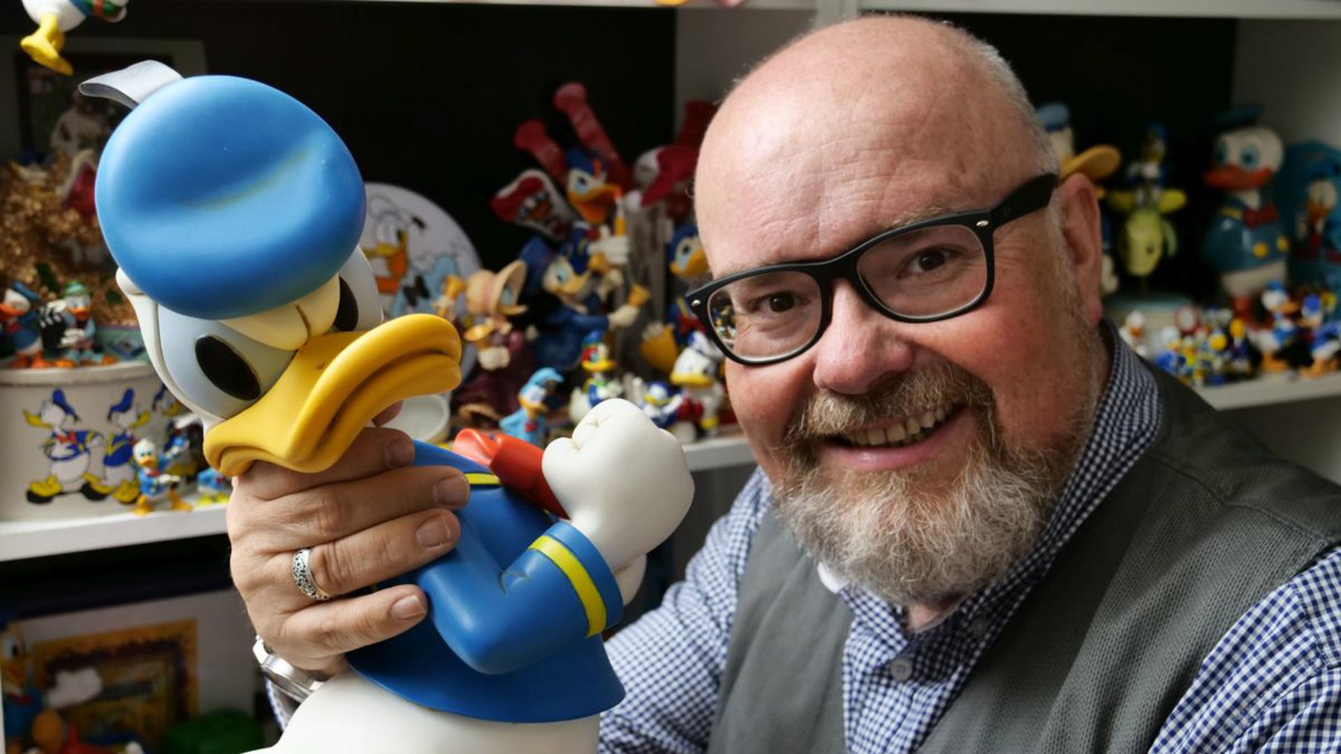 Martin Wacker mit einer Donald Duck Figur vor einem Regal voller Donald Duck Figuren